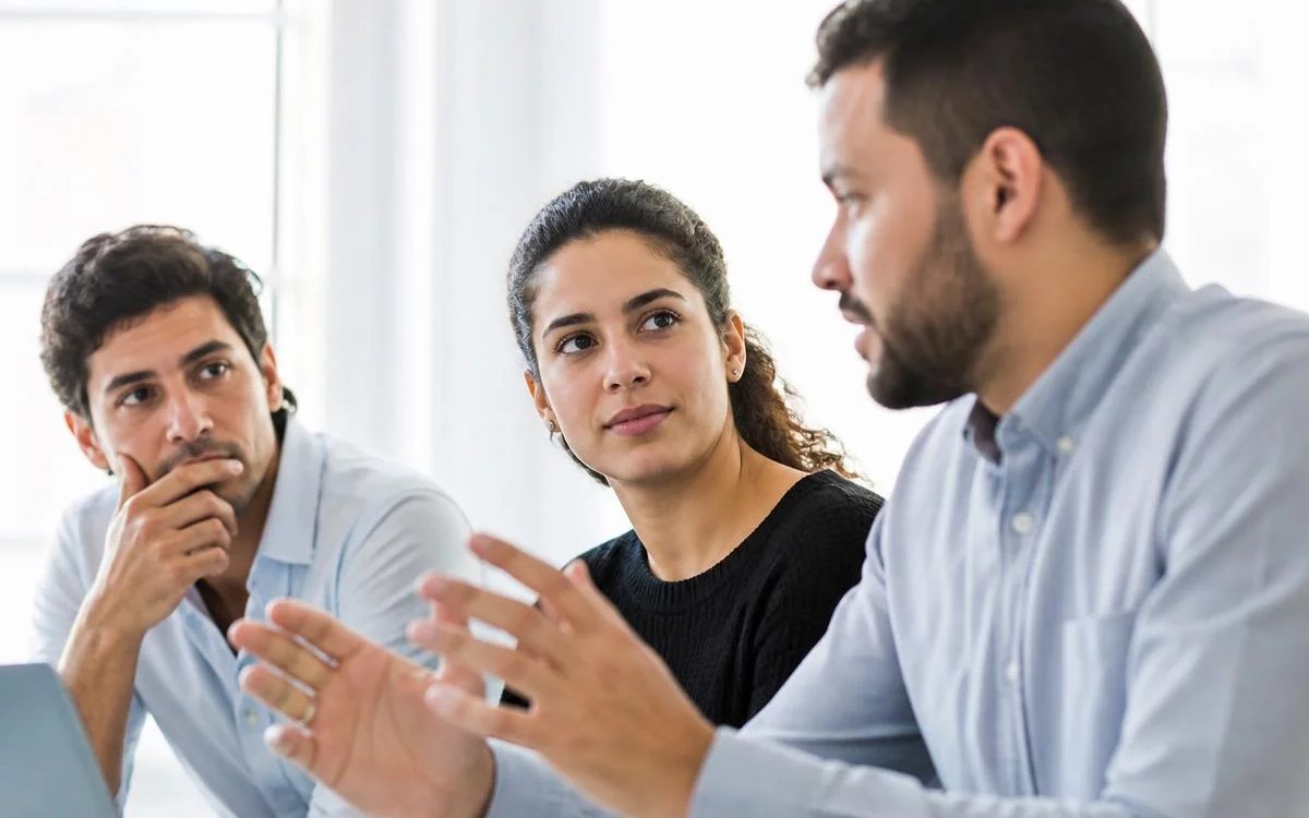 Roda de conversa numa sala clara, com uma pessoa expondo o ponto e duas escutando